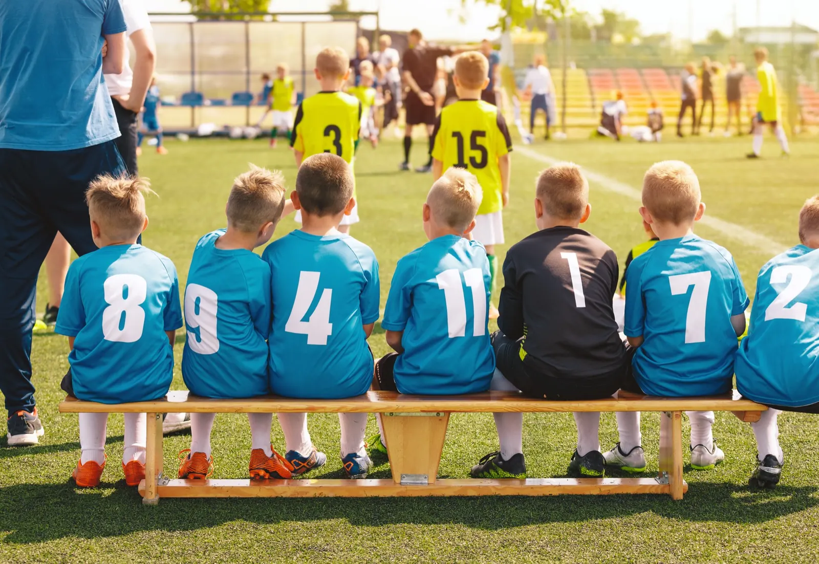 A team of children in blue kit sitting along a bench, watching a match