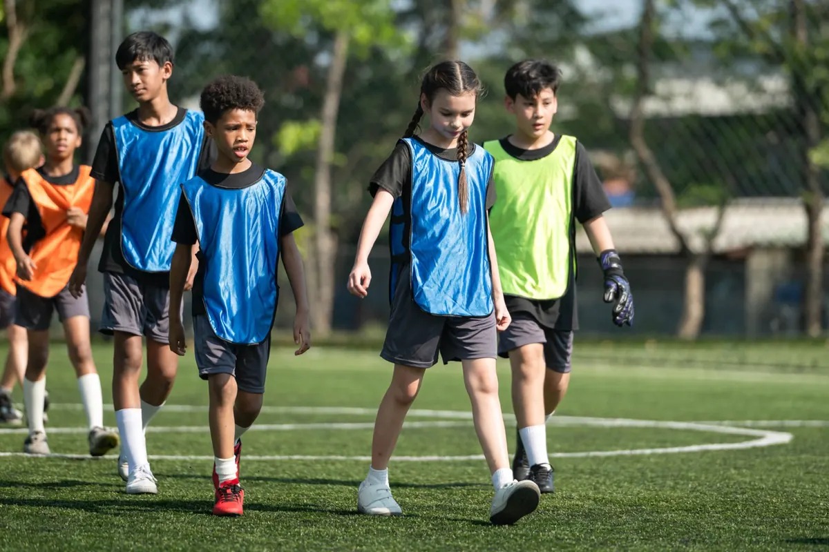A mixed group of children in training bibs walking across the pitch