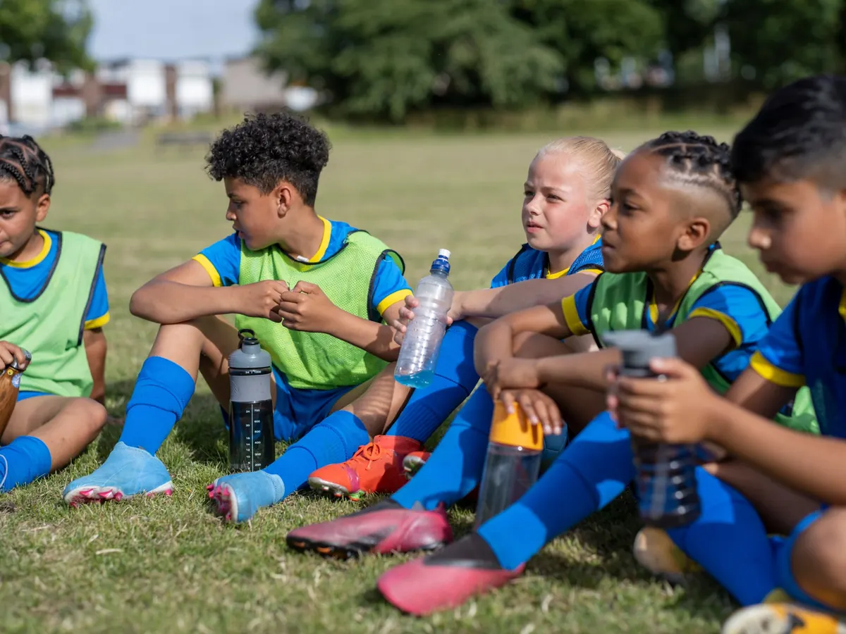 Children in training bibs sitting on the grass at a water break